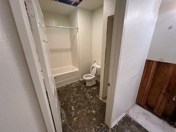 Bathroom with ceiling access cut and heavy water damage staining across the floor