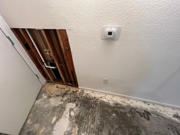 Ceiling access cutout exposing framing and plumbing near a wall thermostat
