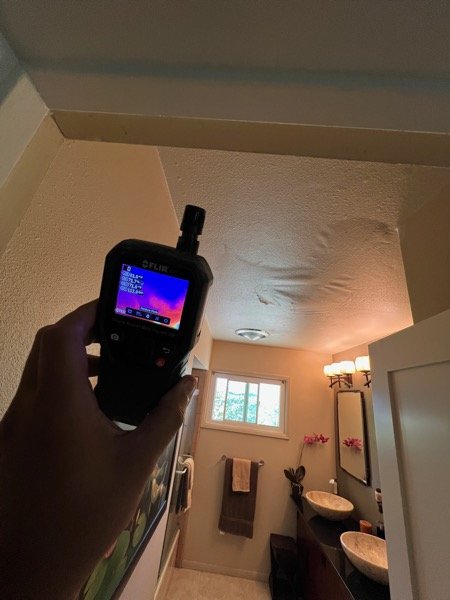Thermal moisture meter reading a visible water stain on a bathroom ceiling