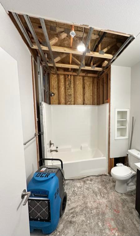 Water-damaged bathroom ceiling opened for inspection with a dehumidifier running